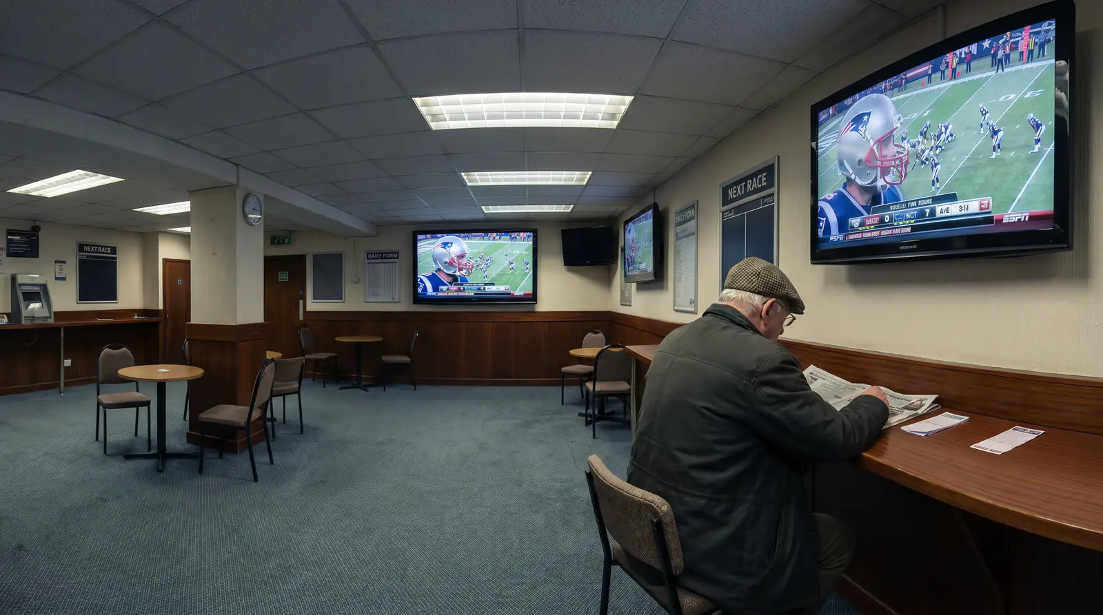 Quiet interior of a long-established UK betting shop with overhead screens showing American football