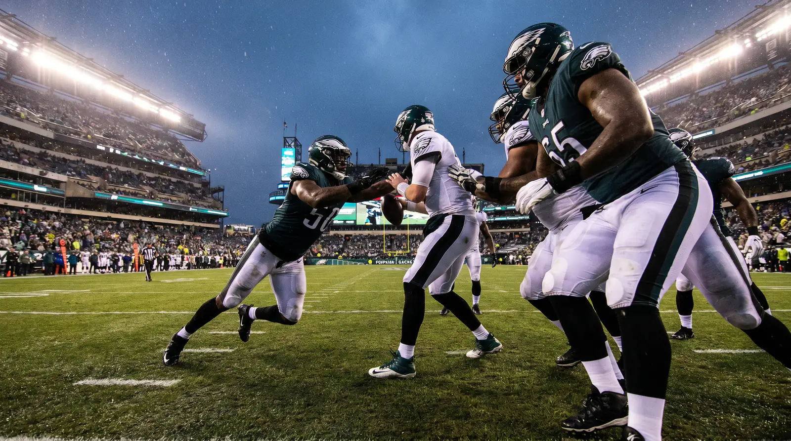 NFL defensive line generating pressure on the quarterback under floodlights