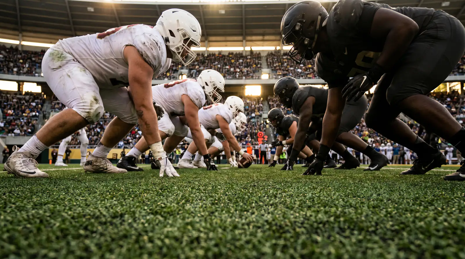 Five American football offensive linemen in three-point stance ready to block at the line of scrimmage